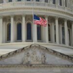 Close-up of the Capitol building in Washington DC with the US flag waving in front.