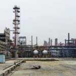 A detailed view of an industrial refinery featuring pipelines and large steel structures.