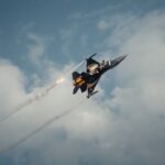 A fighter jet flying through a cloudy blue sky