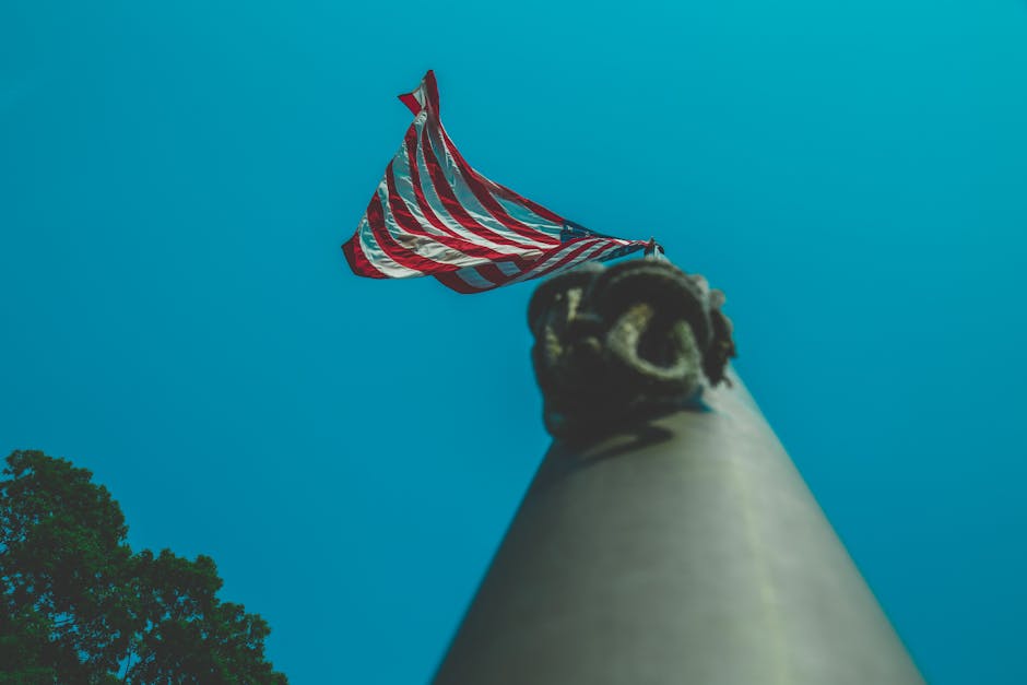 Upward perspective of the American flag on a flagpole against a clear blue sky.