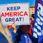 Crowd gathering in Phoenix holding 'Keep America Great' sign at political event outdoors.