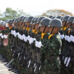 Soldiers in uniform march in a disciplined formation during a military parade outdoors.