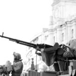 Monochrome image of soldiers in armored tanks, equipped with rifles, patrolling urban surroundings.