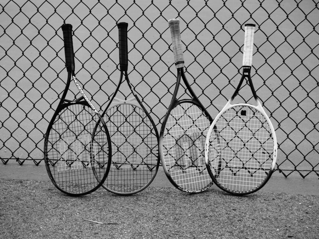 Four tennis rackets lean against a fence.