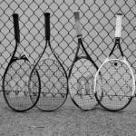 Four tennis rackets lean against a fence.