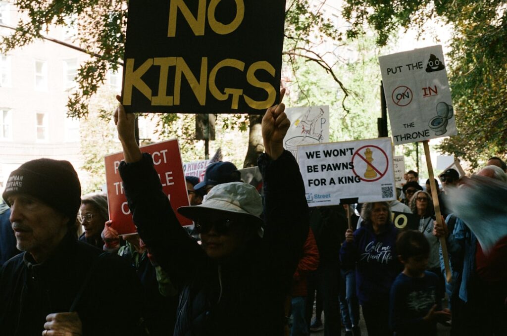 Protesters hold signs with messages against royalty.