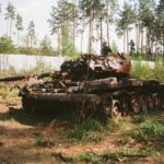 A destroyed military tank lies abandoned in a forest near Bucha, Ukraine amidst war-torn surroundings.