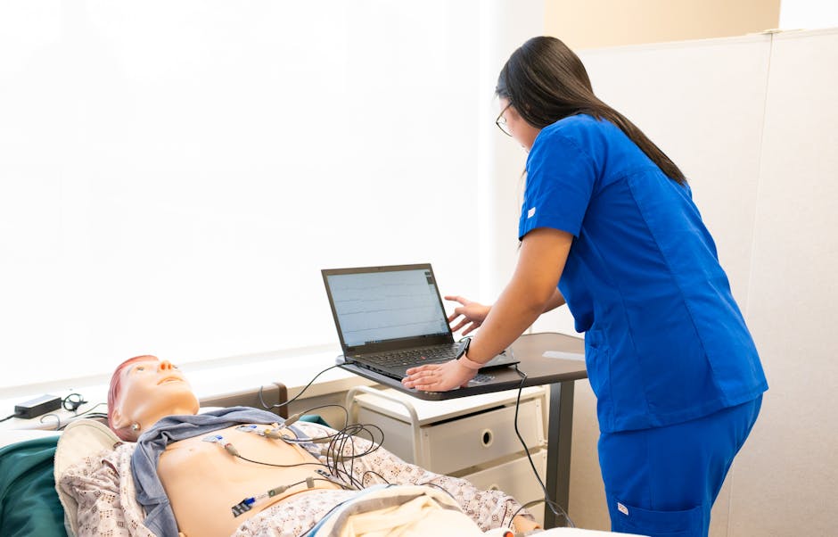 Nurse in training using a laptop with a medical dummy in a clinical simulation lab.