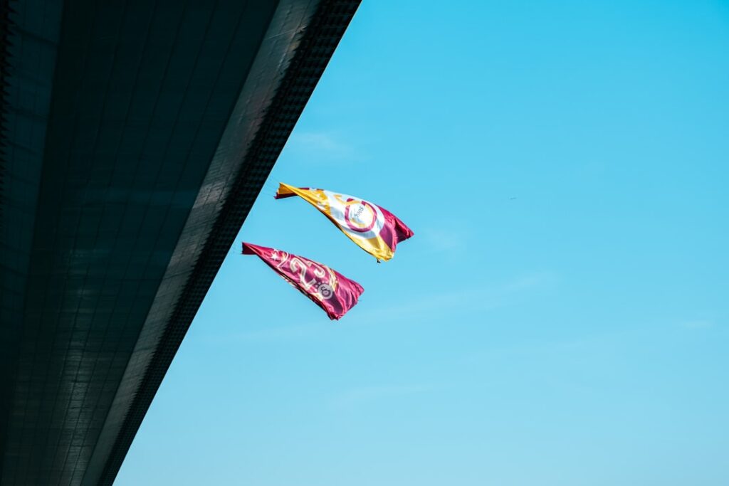 Two flags fly against a clear blue sky.