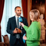 A journalist interviews a professional in a formal setting, highlighting media interaction.