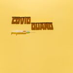 Creative healthcare concept with syringe and 'COVID GUARD' text shadow on yellow background.
