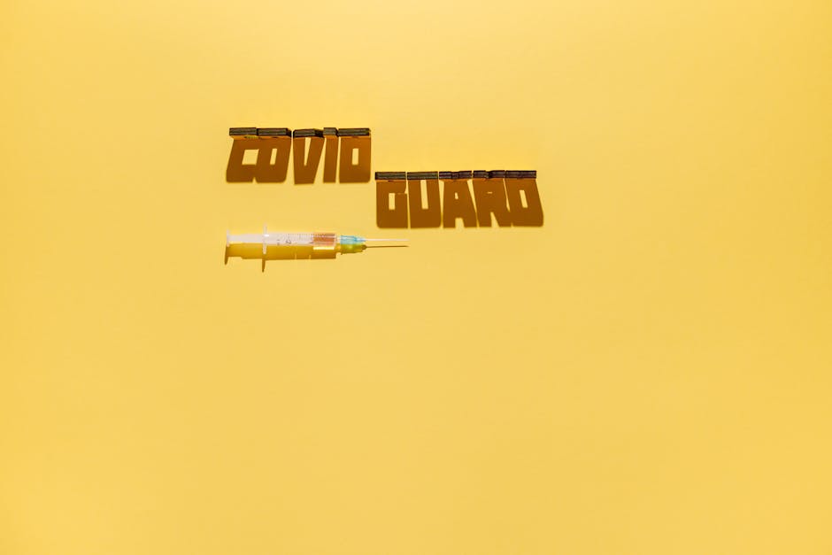 Creative healthcare concept with syringe and 'COVID GUARD' text shadow on yellow background.