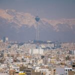 Aerial view of Tehran featuring Milad Tower against the Alborz Mountains.