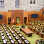 Interior view of the Canadian House of Commons with green seating and wooden decor.