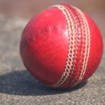 Detailed view of a textured red cricket ball outdoors in sunlight.