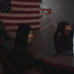 Two masked individuals in a dark room working on computers, symbolizing cyber security threats.