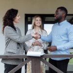 Three adults sealing a real estate deal with a handshake on a porch.