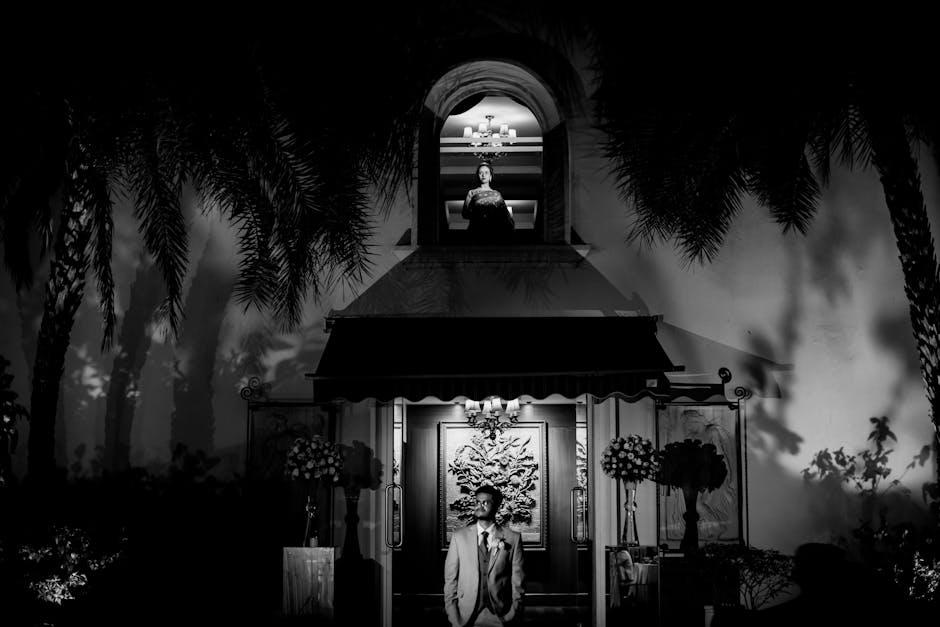 Artistic black and white wedding photo with dramatic lighting, featuring couple in formal attire.