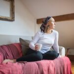 Serene woman in headscarf relaxes on sofa while holding mug, bathed in soft daylight.