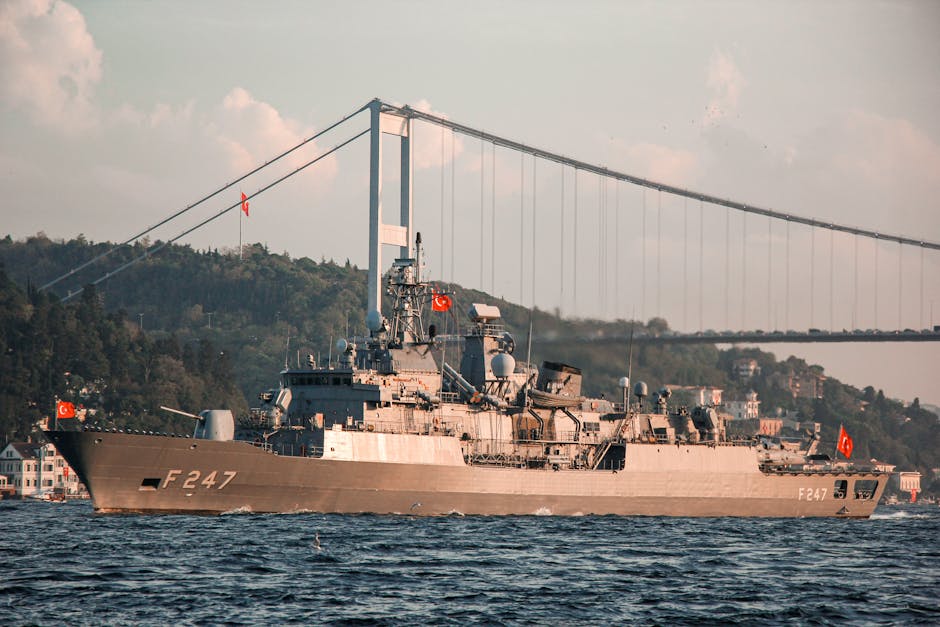 Military vessel with Turkish flags sailing under the Bosphorus Bridge in daylight.