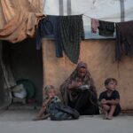 A family outside a tent in a Gaza refugee camp, highlighting daily life and resilience.