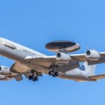 A military AWACS aircraft flying against a clear blue sky, showcasing aerial surveillance capabilities.