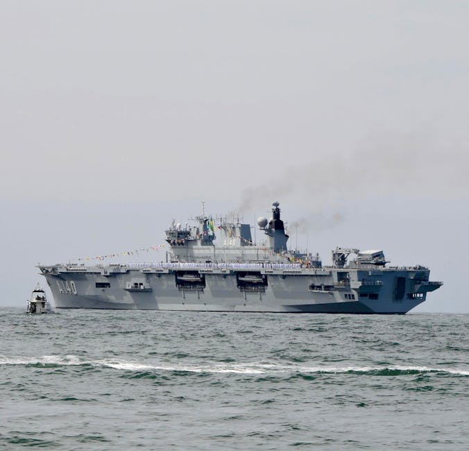 Military aircraft carrier sailing on ocean with visible smoke.