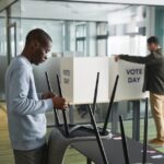 Men preparing voting booths indoors for election day, enhancing democracy.