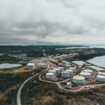 Aerial landscape shot of a coastal oil refinery with storage silos under cloudy skies.