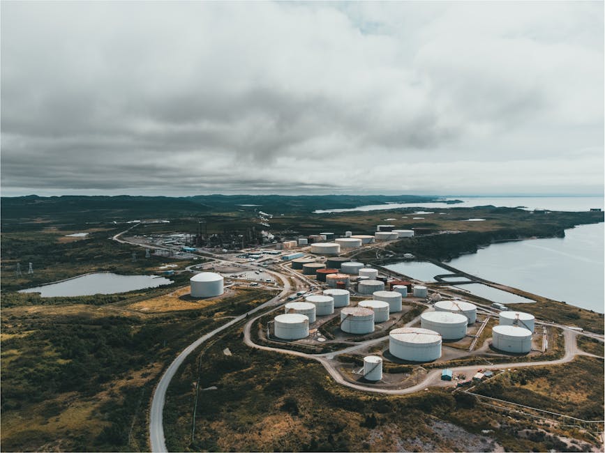 Aerial landscape shot of a coastal oil refinery with storage silos under cloudy skies.