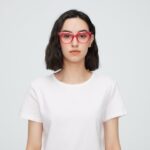 Portrait of a young woman wearing red eyeglasses and a white shirt against a plain background.