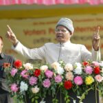 Man delivering a powerful public speech outdoors with a floral adorned podium.