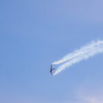 A military jet fighter executing an aerobatic maneuver leaving smoke trails in a clear blue sky.