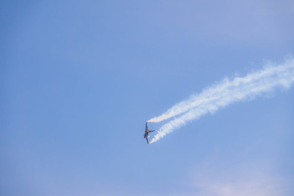 A military jet fighter executing an aerobatic maneuver leaving smoke trails in a clear blue sky.