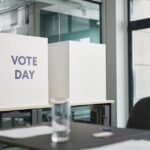 A modern office with voting booths labeled 'Vote Day' indicating election activity.