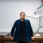 Confident young engineer standing in a laboratory with advanced robotic equipment.