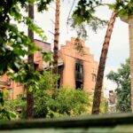 A damaged residential building, charred by fire, stands among lush trees in an urban setting.