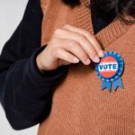 Person wearing a 'Vote' badge, symbolizing participation in democracy and elections.