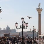 Crowd enjoying sunny day at San Marco Square with iconic columns in Venice, Italy.