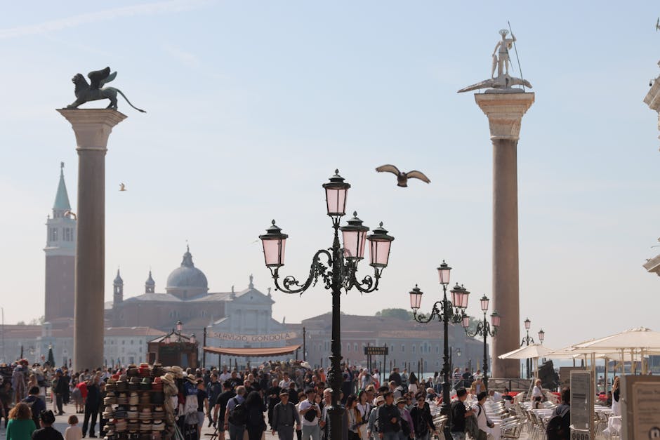 Crowd enjoying sunny day at San Marco Square with iconic columns in Venice, Italy.