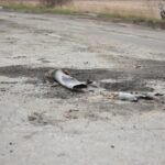 A fragment of a military shell lies on a rural road, depicting destruction.