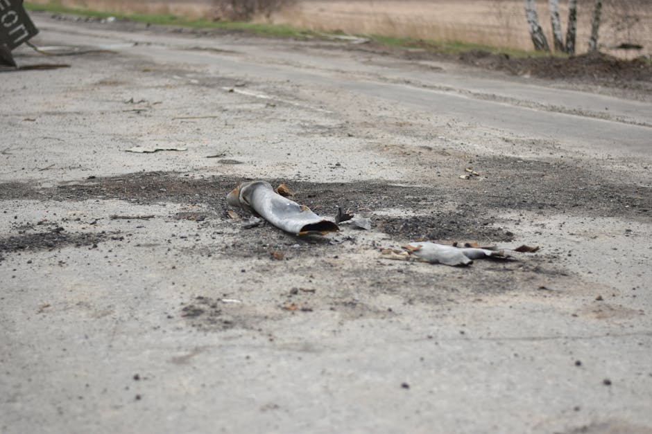 A fragment of a military shell lies on a rural road, depicting destruction.