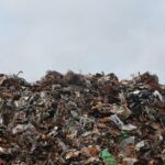 A large pile of scrap metal and waste at a landfill against a cloudy sky.