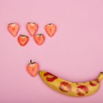 Creative conceptual display using bananas, strawberries on pink background, symbolizing sexuality and romance.