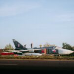 Men explore a Su-24 jet wreckage in a rural field in Belarus.