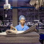 A female worker arranges fabrics in a busy textile factory interior.