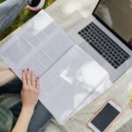 Young woman studying outdoors with laptop, notebook, and smartphone in a park setting.