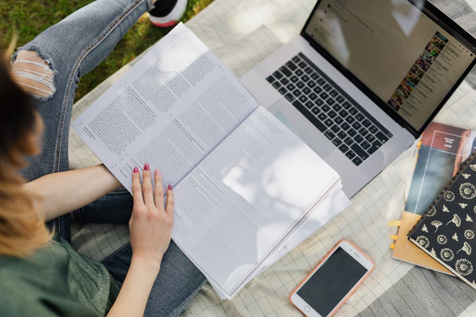 Young woman studying outdoors with laptop, notebook, and smartphone in a park setting.