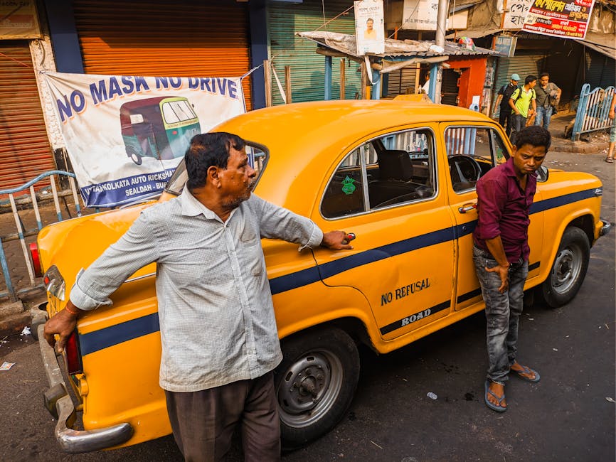 Two men leaning on a classic yellow taxi waiting on a street in Kolkata, India.