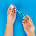 Hands holding a syringe and COVID-19 vaccine vial on a blue background.